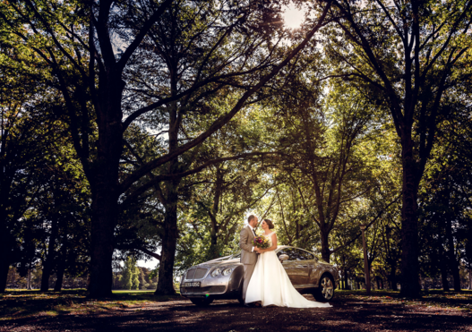 Bride and groom posing in forest with limo